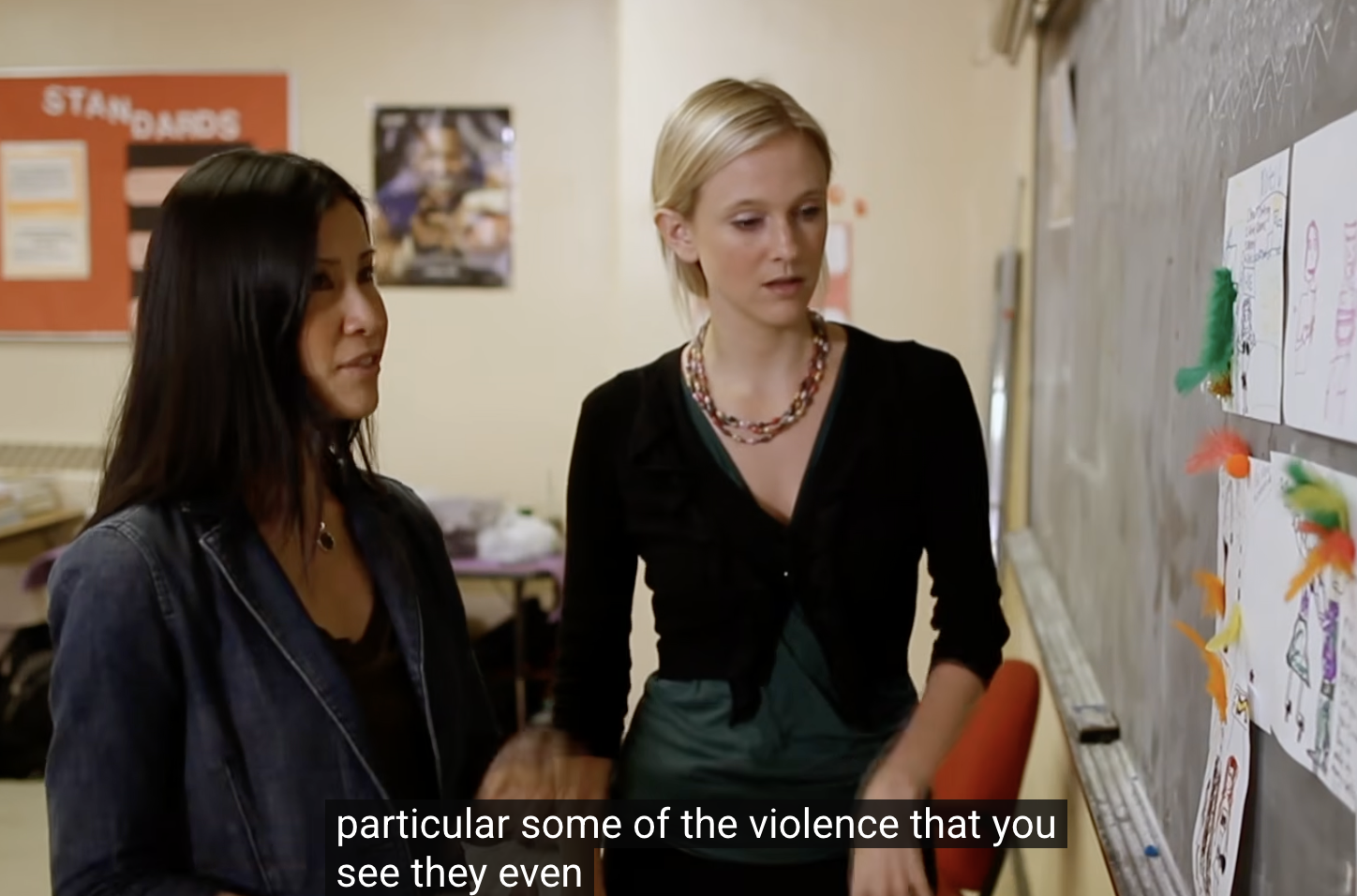 Andrea Powell and Lisa Ling in conversation at a chalkboard covered with survivors' drawings