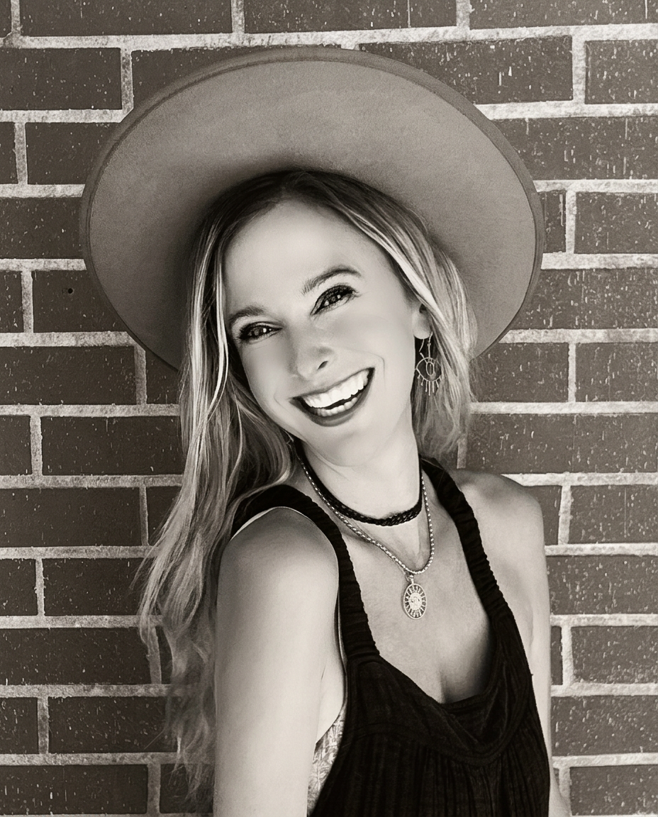 Warm-toned black and white portrait of Andrea smiling in a wide-brim hat
